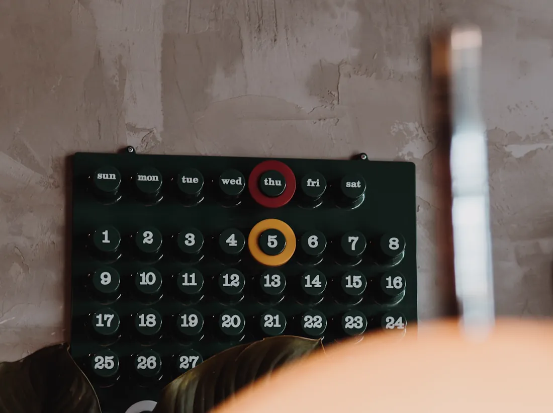A wall-mounted calendar board with the day and date dialled in